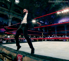 a man in a suit and tie is walking in a wrestling ring with a w logo on the side