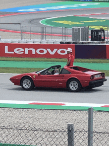 a red ferrari is driving on a race track with a lenovo sign behind it