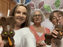 three women wearing bunny ears are holding chocolate bunny heads