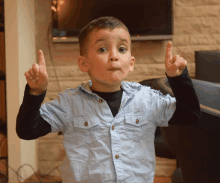 a young boy in a blue shirt holds up his fingers