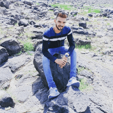 a man sitting on a rock in a field with a watch on his wrist