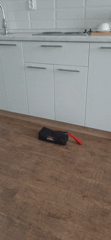 a black bag with a red handle sits on a wooden floor in a kitchen