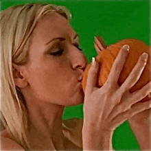 a woman is kissing a pumpkin against a green background .