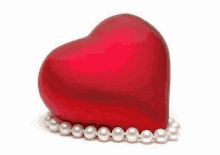 a red heart sitting on top of a string of pearls .