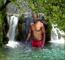 a shirtless man stands in front of a waterfall