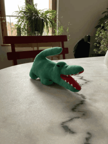 a green stuffed crocodile with red teeth sits on a white table