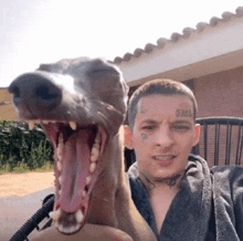 a man with a tattoo on his face holds a dog with its mouth wide open