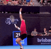 a man in a red shirt is jumping in the air while holding a tennis racquet in front of a brisbane sign