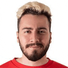 a man with a beard and blonde hair is wearing a red shirt and looking at the camera .