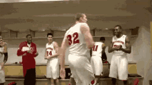 a group of basketball players are standing in a locker room . one player has the number 32 on his jersey .