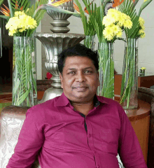 a man in a pink shirt is sitting in front of a vase of flowers