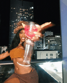 a woman is holding a large martini glass in front of a city skyline at night