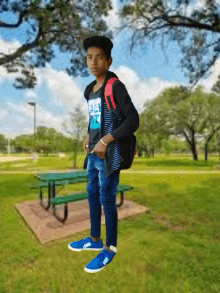 a boy with a backpack is standing in a park near a picnic table