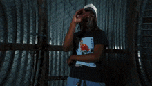 a man standing in front of a chain link fence wearing a black t-shirt with a picture of a bird on it