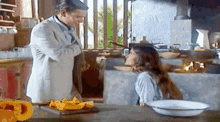 a man and a woman are standing next to each other in a kitchen with a bowl of food on the table .