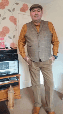 a man wearing a plaid shirt and a vest stands in front of a stereo