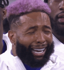 a man with purple hair and a beard is crying while sitting in the stands .