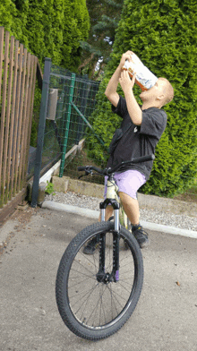 a young boy drinking from a bottle while riding a bicycle