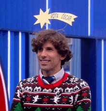 a man wearing a christmas sweater and tie has a star on his head that says vota oscar