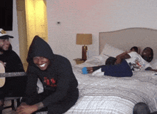 a man in a black hoodie is sitting on a bed next to two other men