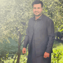 a man wearing a black vest and a black shirt stands in front of a tree