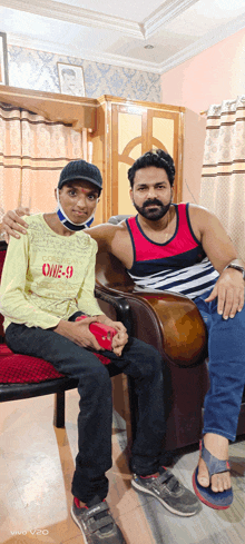 a man sitting next to a boy wearing a yellow shirt that says one-9