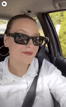 a woman in a car wearing sunglasses and a white shirt