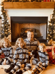 a man and three children sit in front of a fireplace wearing pajamas