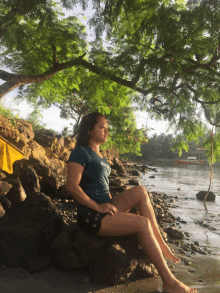 a woman is sitting on a rock near the water