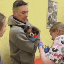 a man is holding a small dog in his arms while a woman in a scrub top with cats on it looks on