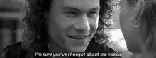 a black and white photo of a man with curly hair smiling and talking to a woman .