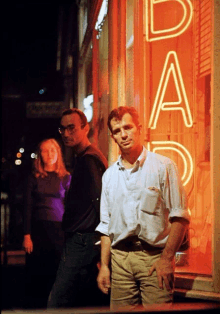 a man stands in front of a neon sign that says ' dad '