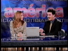 a man and a woman are sitting at a desk in front of a sign that says america noticias