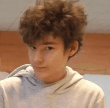 a young man with curly hair wears a grey hoodie