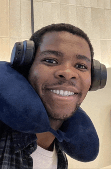 a man wearing headphones and a blue neck pillow smiles