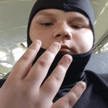 a young boy wearing a black hood holds his hand up to his face