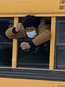 a man wearing a mask looks out the window of a yellow bus