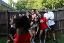 a group of people standing in front of a wooden fence with one girl wearing a red shirt with an american flag on it