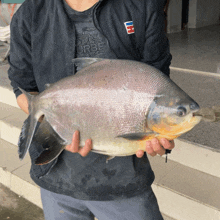 a person holding a large fish wearing a black jacket with the word urban on it