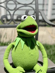 a kermit the frog puppet sits on a chair