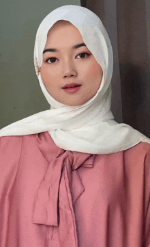 a woman wearing a pink shirt and a white hijab looks at the camera