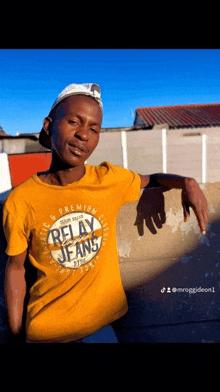 a man wearing a yellow relay jeans t-shirt is leaning against a wall