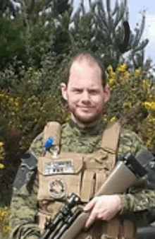 a man in a military uniform is holding a rifle in front of a bush .