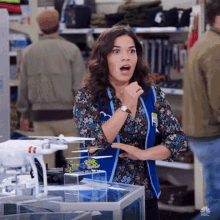 a woman is standing in front of a display of drones in a store and making a surprised face .