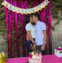 a man and a woman kissing in front of a happy birthday banner