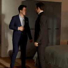 two men in suits standing next to each other in front of a bed