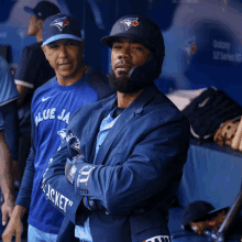 a man wearing a blue jays jacket is standing in the dugout