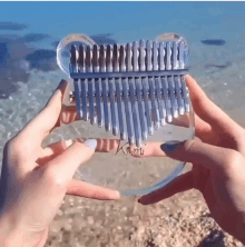 a person is holding a clear kalimba in front of the ocean