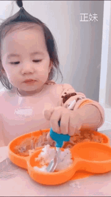 a little girl is sitting at a table with a plate of food and a spoon in her hand .