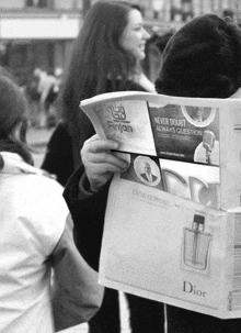 a man is reading a newspaper with an ad for dior homme on it